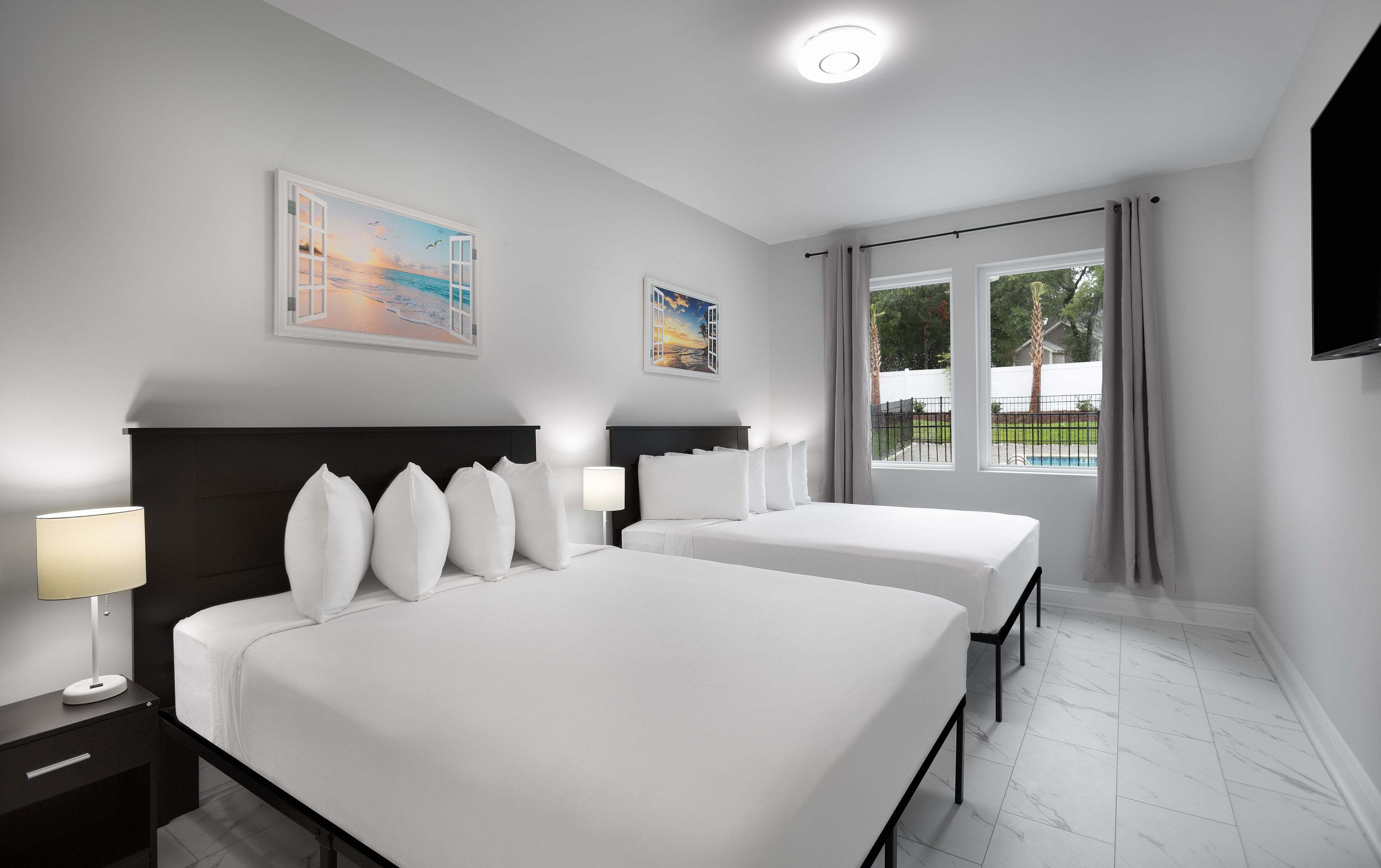 A hotel room with two beds, a large window with a view of the outdoors, and artwork on the walls.