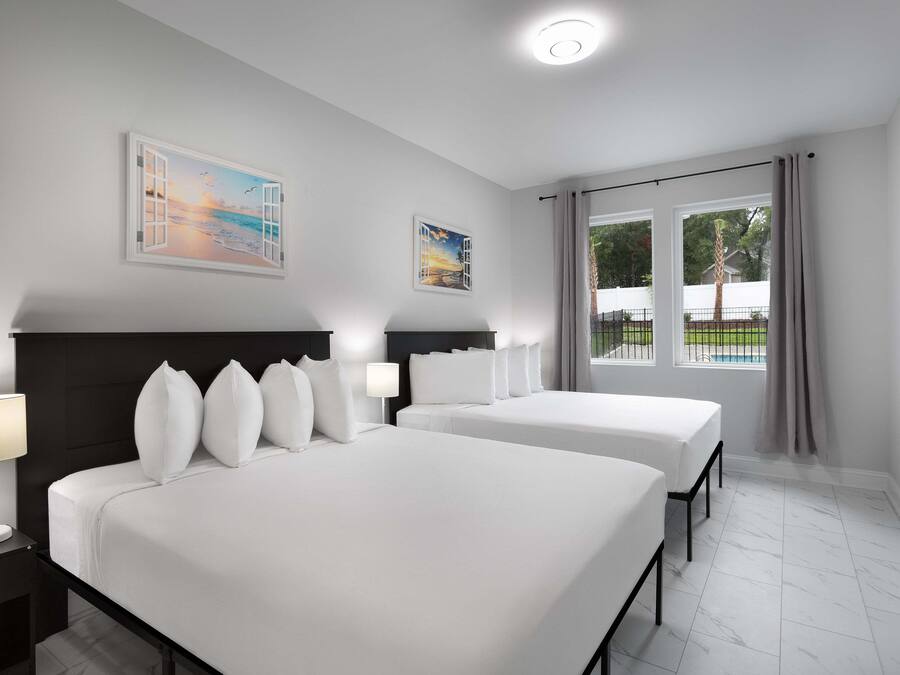 A hotel room with two beds, a large window with a view of the outdoors, and artwork on the walls.