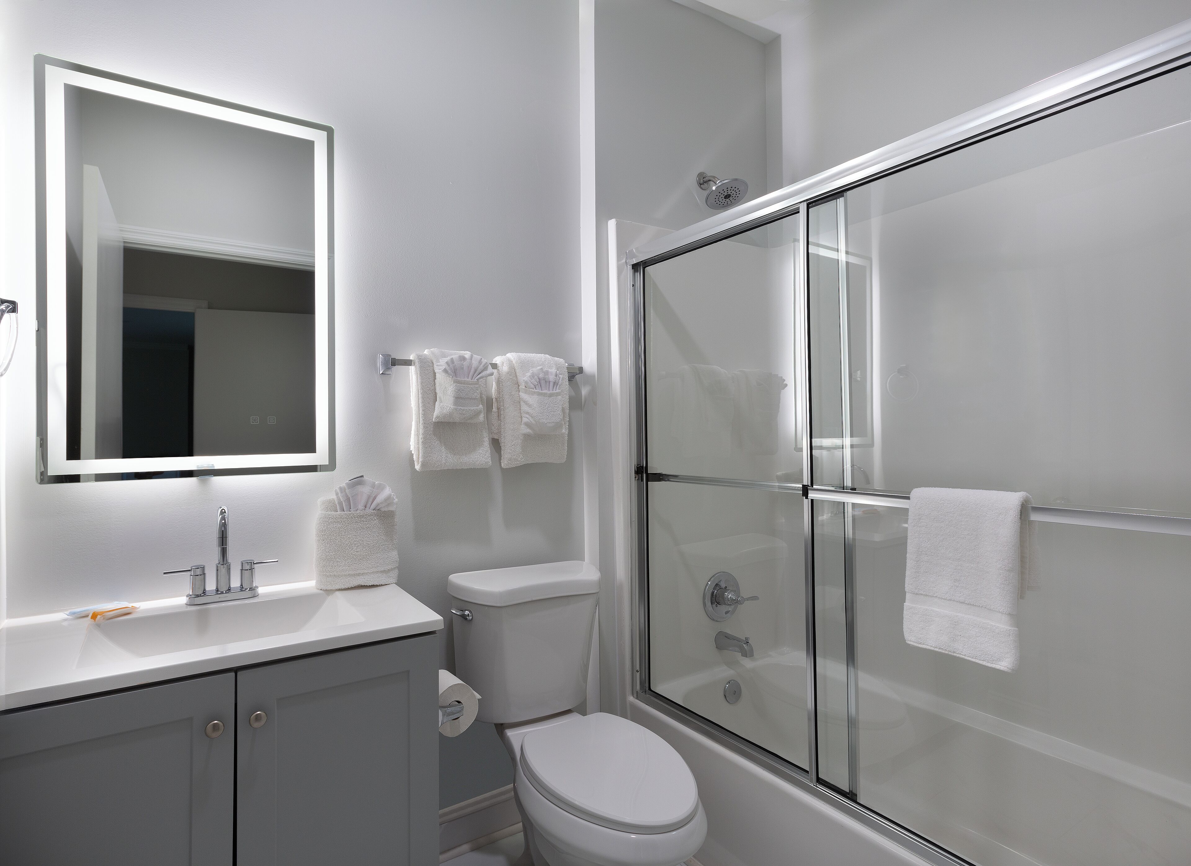 Une salle de bain moderne avec une douche à parois de verre, des toilettes blanches et un meuble-lavabo avec un miroir.