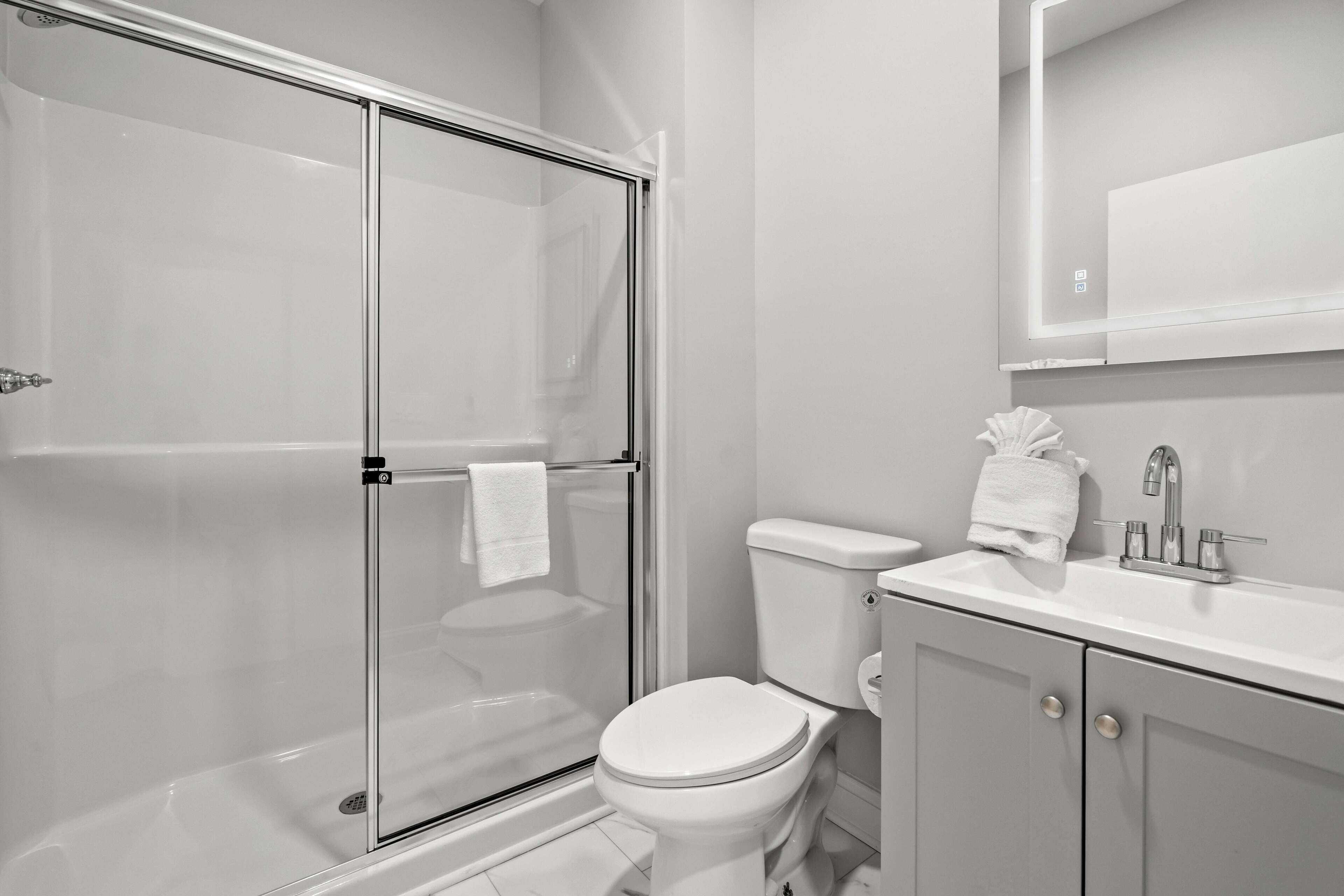 Un baño moderno con ducha de vidrio, inodoro blanco y lavabo con espejo superior.