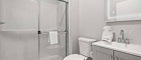 Un baño moderno con ducha de vidrio, inodoro blanco y lavabo con espejo superior.