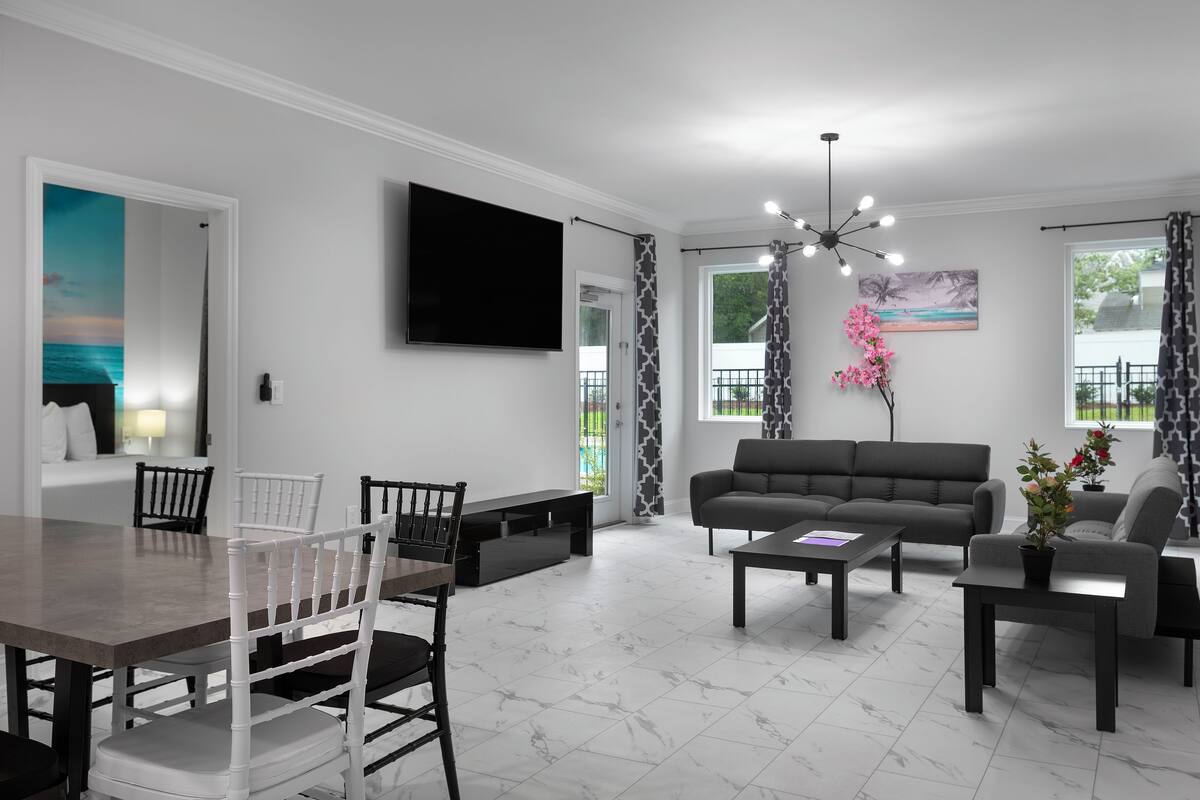 Una sala de estar moderna con comedor, un sofá gris, una mesa de centro y un televisor montado en la pared.