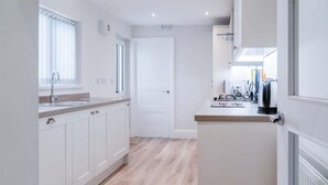A modern kitchen with white cabinetry, a wooden countertop, and a view of the adjacent living area. - Fleet Street - 2 Bedroom Holiday Home - Swansea (Swansea)