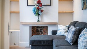 A modern living room with a grey sectional sofa, a fireplace, and a wall-mounted shelf. - Fleet Street - 2 Bedroom Holiday Home - Swansea (Swansea)