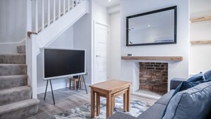 A modern living room with a staircase, a flat-screen TV, a fireplace, and a sofa. - Fleet Street - 2 Bedroom Holiday Home - Swansea (Swansea)
