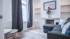 A modern living room with a grey sofa, a small round table, and a fireplace. - Fleet Street - 2 Bedroom Holiday Home - Swansea (Swansea)