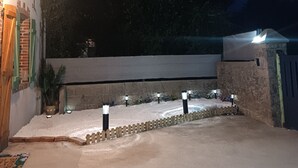 A nighttime view of a residential area with a paved driveway, a white wall, and a wooden fence.