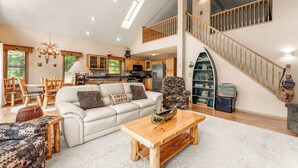 A spacious living area with a high ceiling, a wooden staircase, and a cozy seating arrangement including a sofa and chairs.