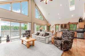 Ein geräumiges Wohnzimmer mit großem Fenster, einer Couch, einem gemusterten Sessel und einem Couchtisch aus Holz.