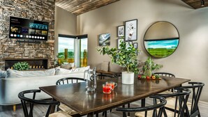 A modern living room with a stone wall, a fireplace, a flat-screen TV, a dining table with chairs, and a large window offering a view of the outdoors. - Luxury Log Home with a Hot Tub. (Selfoss)
