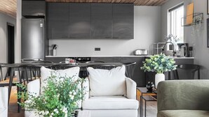 A modern kitchen with dark cabinets, a large island, and a dining area with a white sofa and a green armchair. - Luxury Log Home with a Hot Tub. (Selfoss)