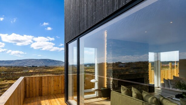 A modern building with large glass windows, wooden deck, and a seating area with cushions. - Luxury Log Home with a Hot Tub. (Selfoss)