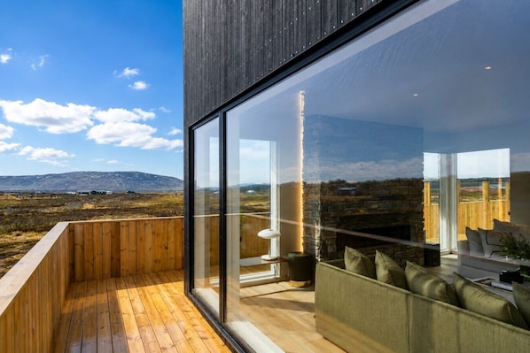 A modern building with large glass windows, wooden deck, and a seating area with cushions.