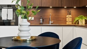 A modern kitchen with dark wooden cabinets, a white countertop, and a round dining table with blue chairs.