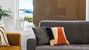 A modern living room with a grey sofa, a mustard-colored armchair, and a large window with blinds.