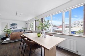 A modern living room with a wooden dining table, comfortable seating, large windows, and a view of the city. - Down Town RVK. Shopping Street Living (Reykjavík)