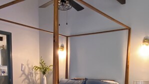 Uma cama de dossel com um edredom estampado com flores, uma mesa de cabeceira com abajur e um ventilador de teto.