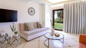 Un salon moderne avec un canapé, une table basse ronde, un téléviseur à écran plat et une grande fenêtre avec des rideaux.