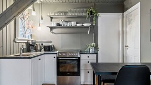 A compact kitchen with white cabinets, a stainless steel stove, and a dining table with a black chair.