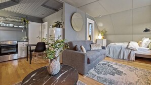 A modern living room with a grey sofa, a round mirror, and a dining area with a table and chairs.