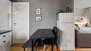A compact living space with a kitchenette, a dining area with a table and chairs, a white refrigerator, and a bed with a grey headboard.