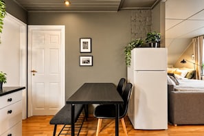 A compact kitchen with a dining table, chairs, a refrigerator, and a bench.