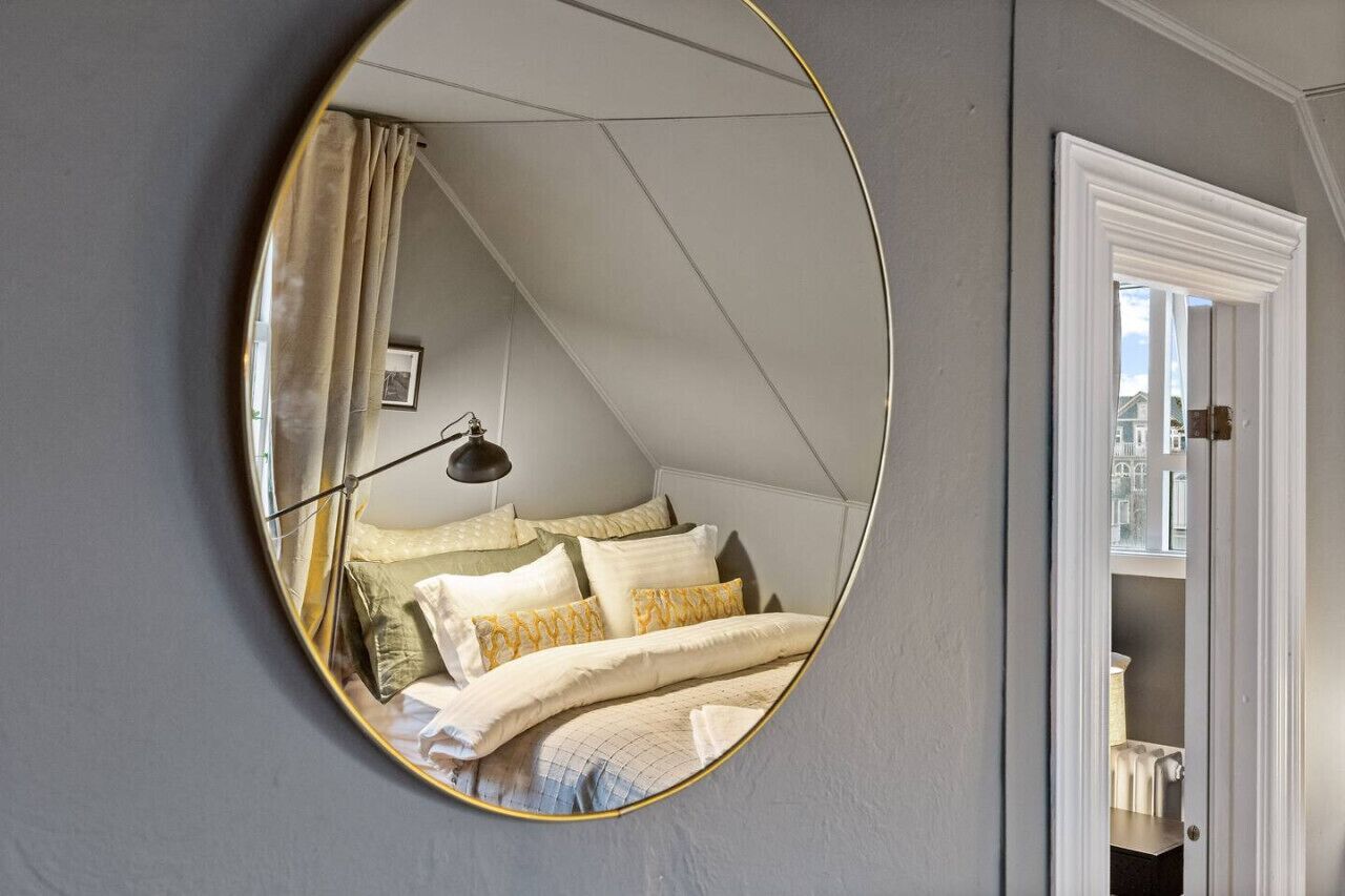 Ein Schlafzimmer mit einem runden Spiegel, der ein Bett, eine Lampe und ein Fenster widerspiegelt.
