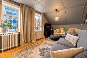 A modern living room with a sofa, a television, and a large window with curtains. - Cultural Gem in the Heart of Central Reykjavík (Reykjavík)