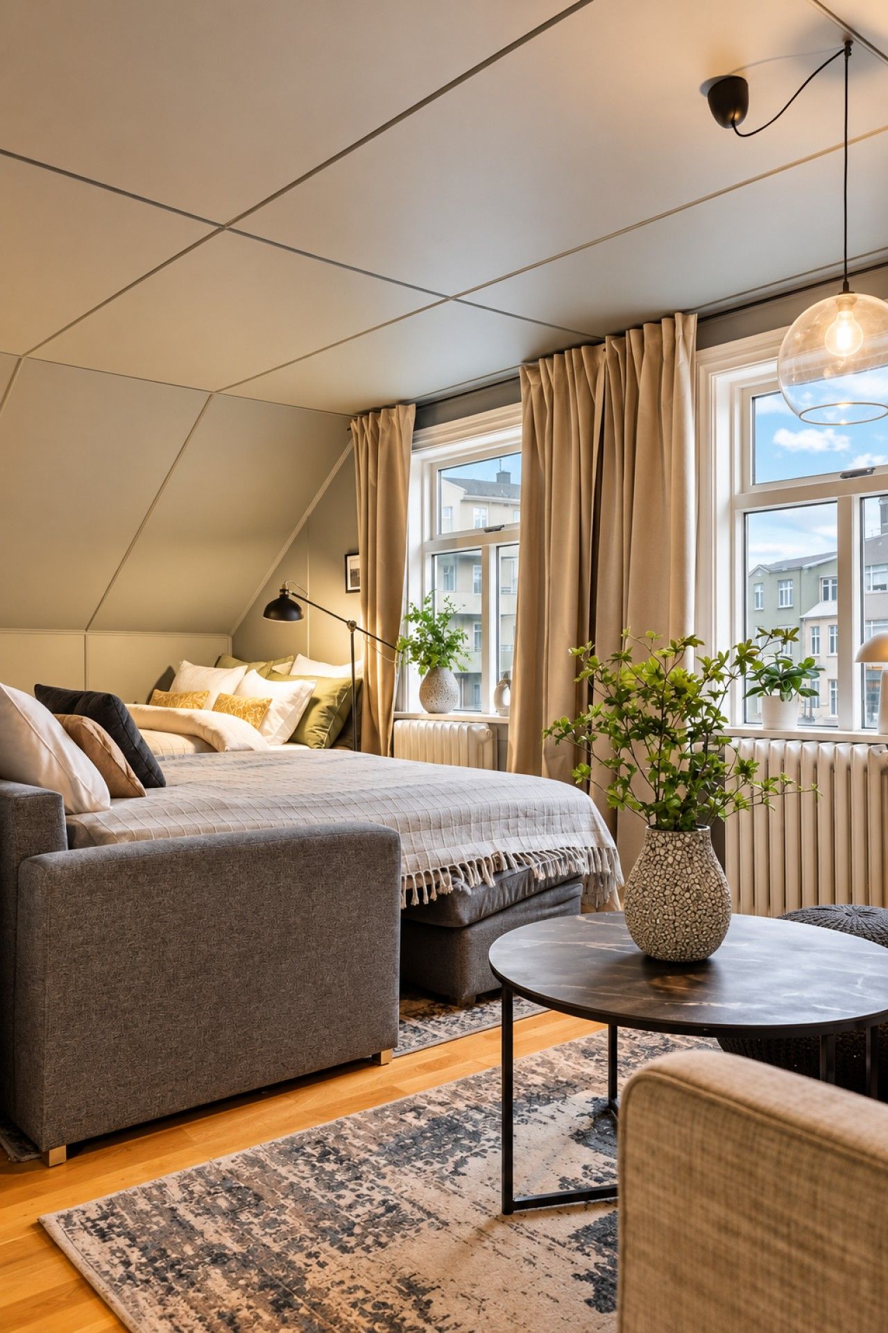 A modern bedroom with a loft-style bed, a sofa, a round coffee table, and a potted plant.