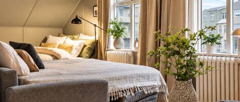 A modern bedroom with a loft-style bed, a sofa, a round coffee table, and a potted plant.