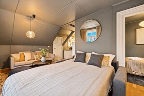 A modern bedroom with a large bed, a sofa, a round mirror, and a view of a staircase.