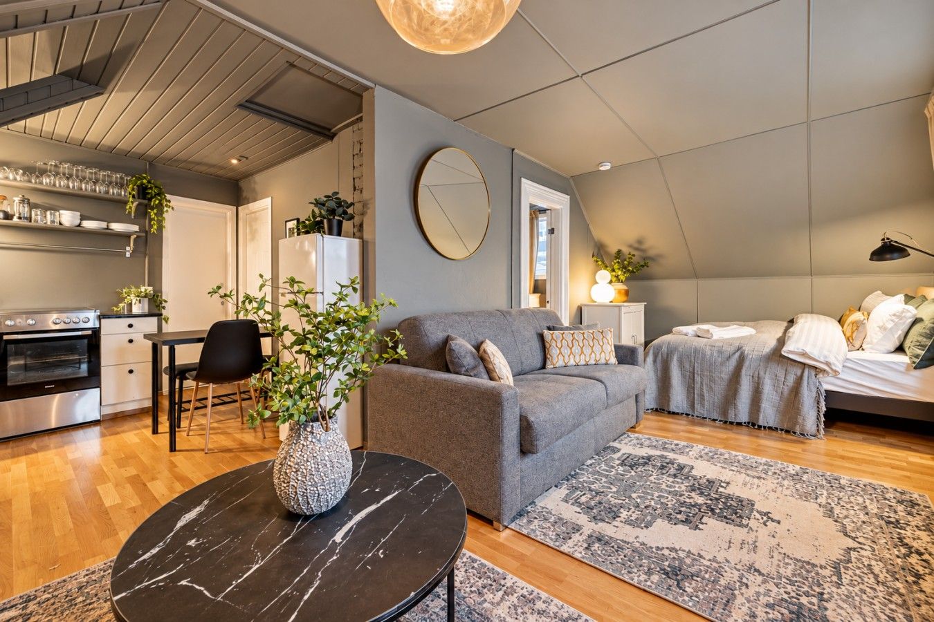 Ein modernes Wohnzimmer mit einer Couch, einem Essbereich mit Tisch und Stühlen, einer Küche mit Backofen und einem großen Spiegel an der Wand.