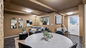 Ein modernes Wohnzimmer mit einem runden Esstisch, einem grauen Sofa und einem großen Fenster.