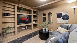 Ein modernes Wohnzimmer mit großem Flachbildfernseher, Holzregalen, einer Couch und einem Couchtisch.
