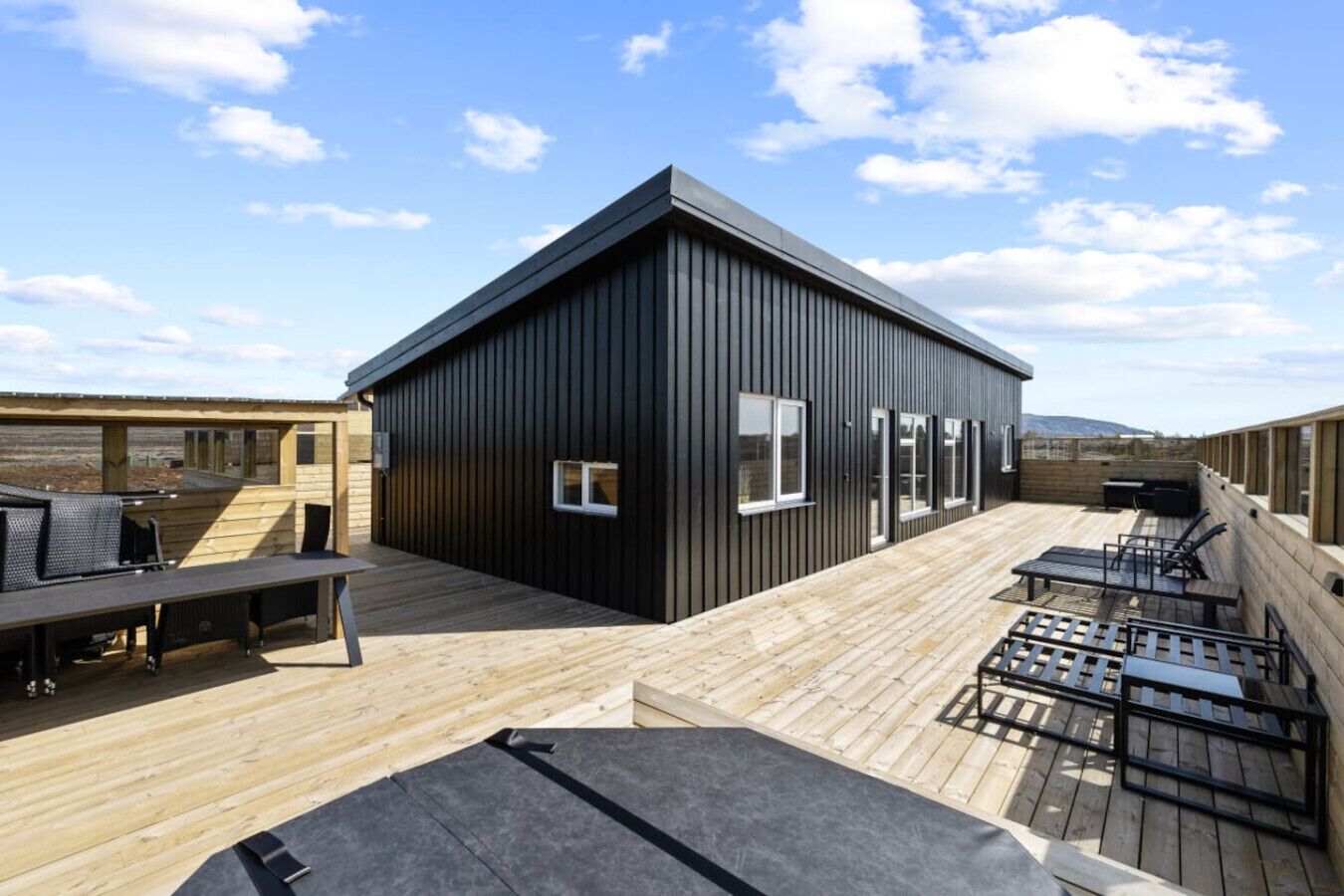 A modern building with a flat roof, large windows, and a wooden deck with outdoor furniture.