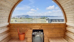 Une cabane en bois dotée d’une grande fenêtre en arc de cercle, d’un banc en bois et d’un seau.