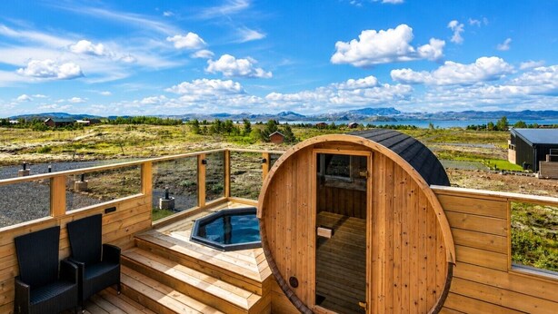 Une terrasse en bois avec un sauna, un espace salon extérieur et une vue sur les montagnes et un lac.