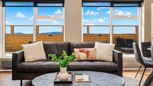 Un salon moderne avec un canapé en cuir, une table basse ronde et une vue sur les montagnes grâce à de grandes fenêtres.