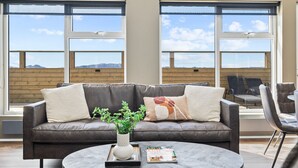 A modern living room with a leather sofa, a coffee table, and a view of mountains through large windows.