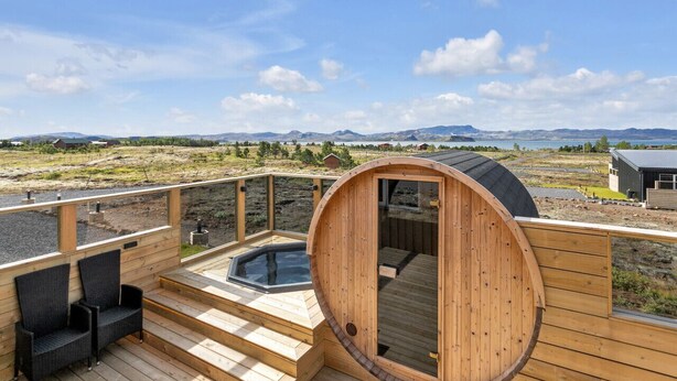 A wooden deck with a hot tub, seating area, and a sauna.