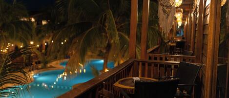 A poolside area with a wooden deck, chairs, and a view of a swimming pool.