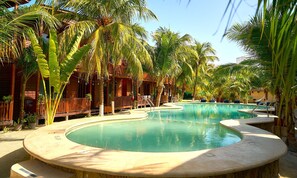 A pool area with palm trees, wooden deck, and a building with balconies. - Coconut by ÓOL Hotels (Isla Holbox)