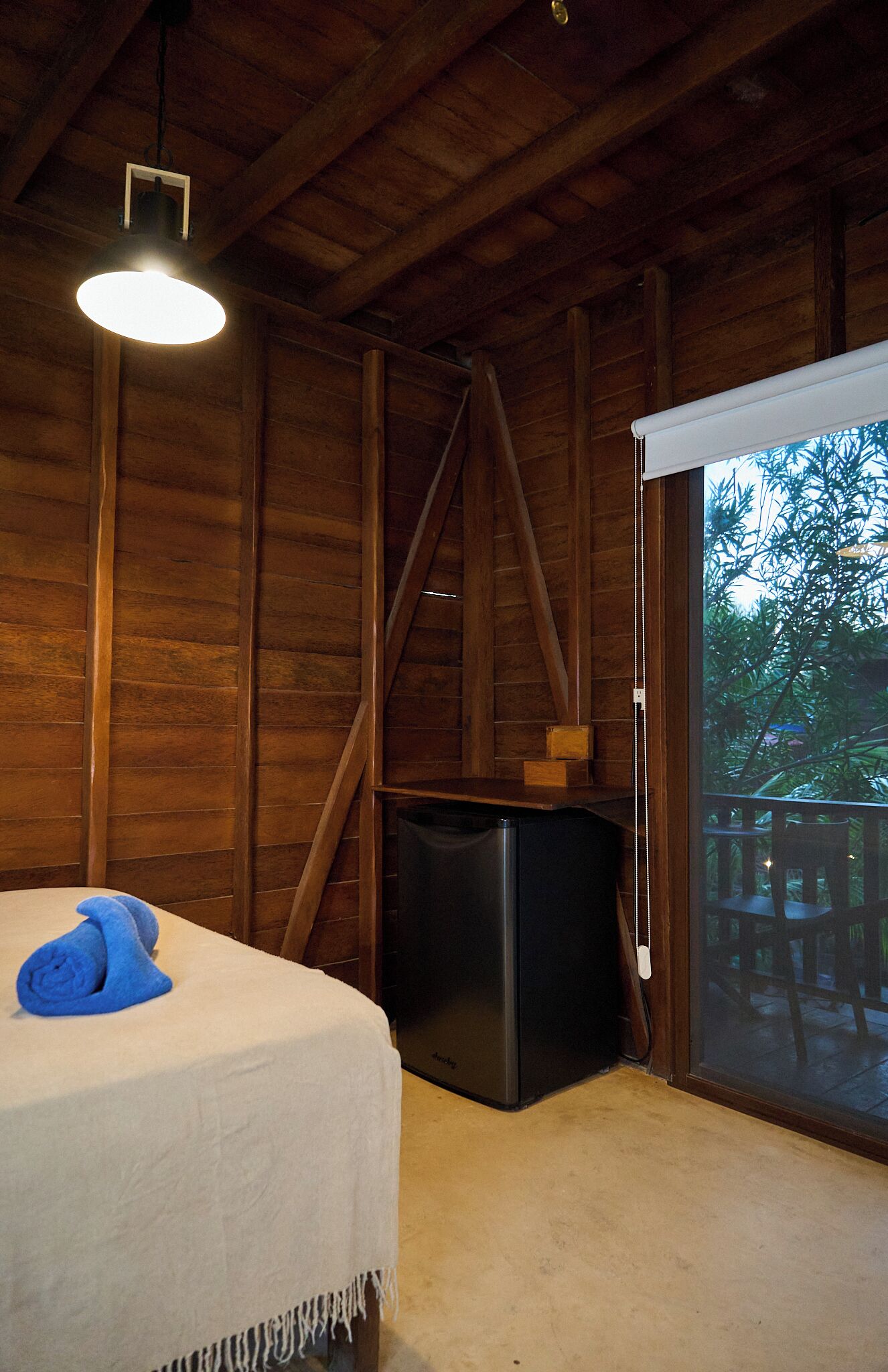 Habitación de cabaña de madera con una cama, un electrodoméstico negro pequeño y una ventana con vistas a árboles.