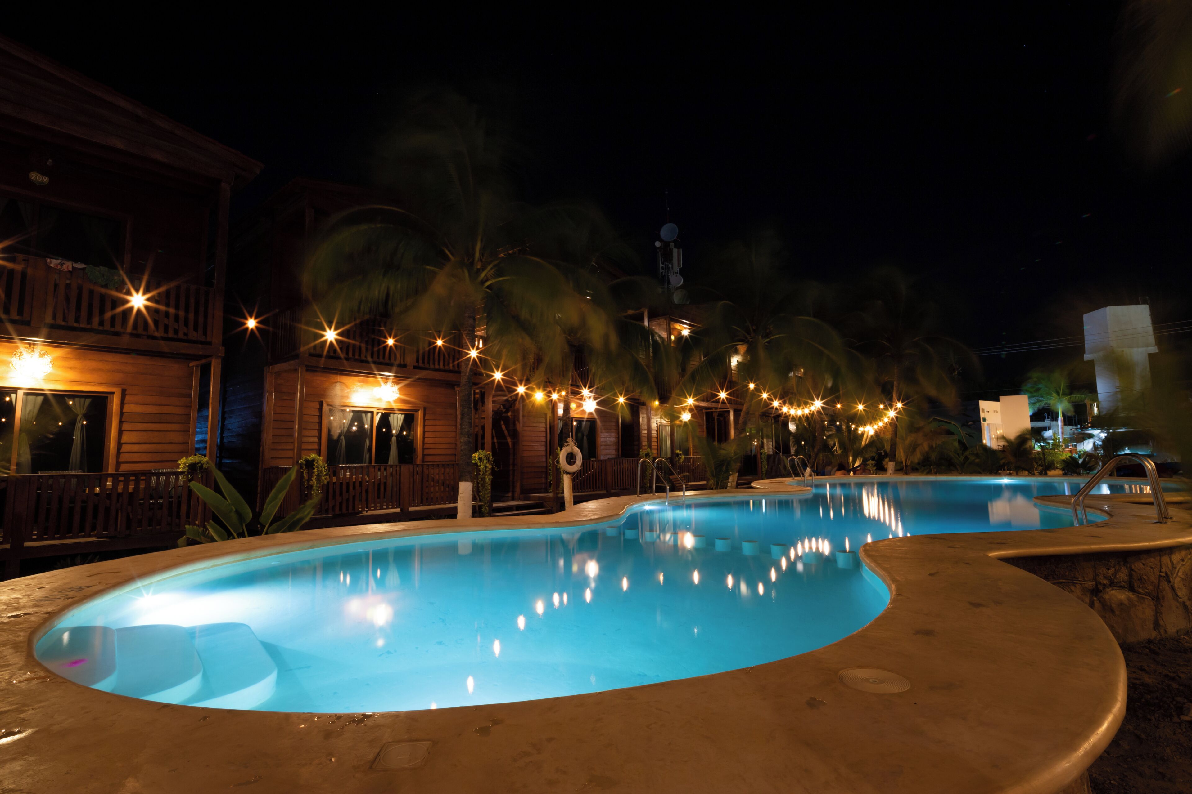 A nighttime swimming pool area with a wooden deck and string lights.