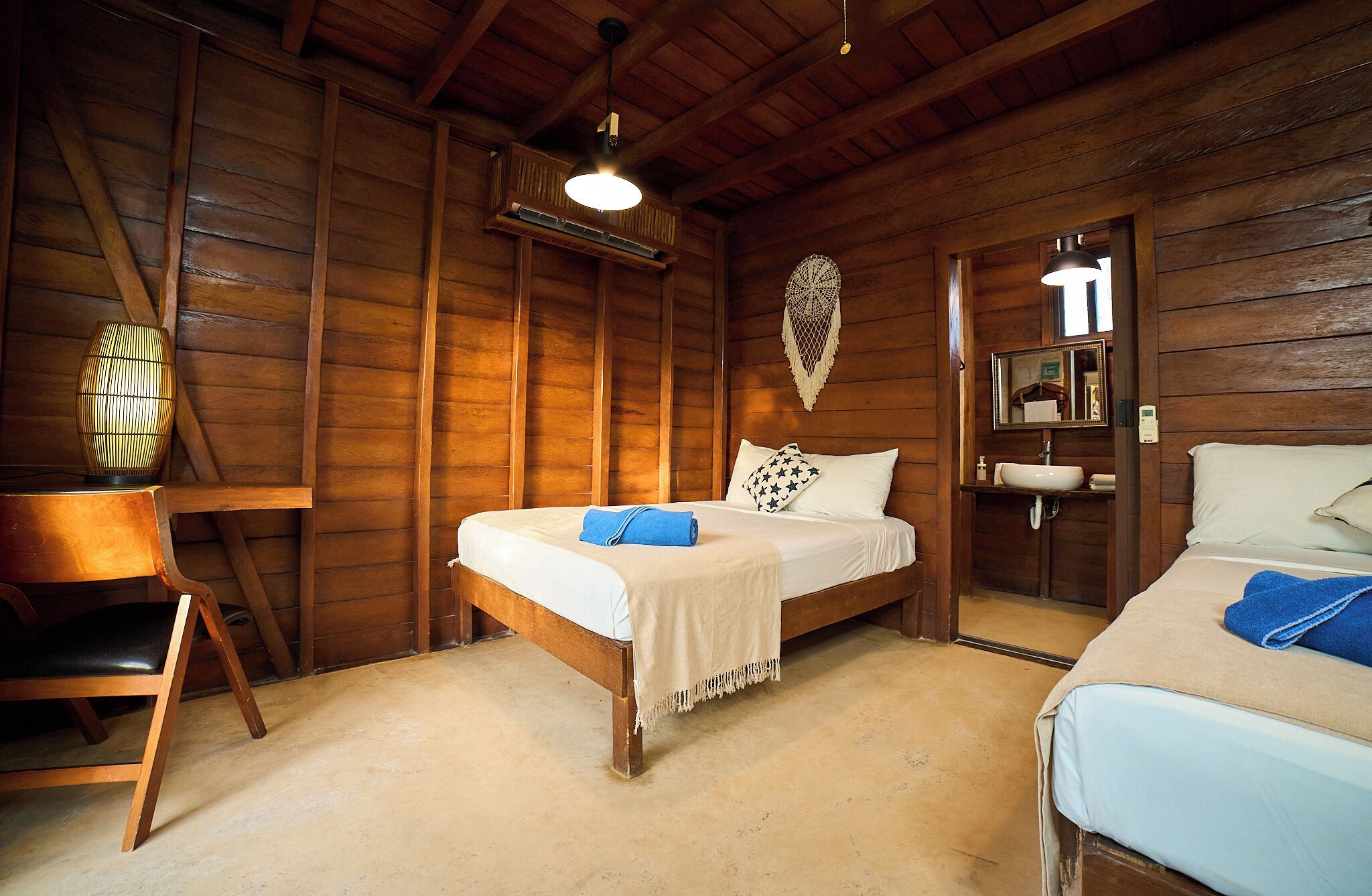 Ein holzgetäfeltes Zimmer im Blockhausstil mit zwei Betten, einem Schreibtisch, einem Stuhl, einer Pendelleuchte und einem wandmontierten Spiegel.