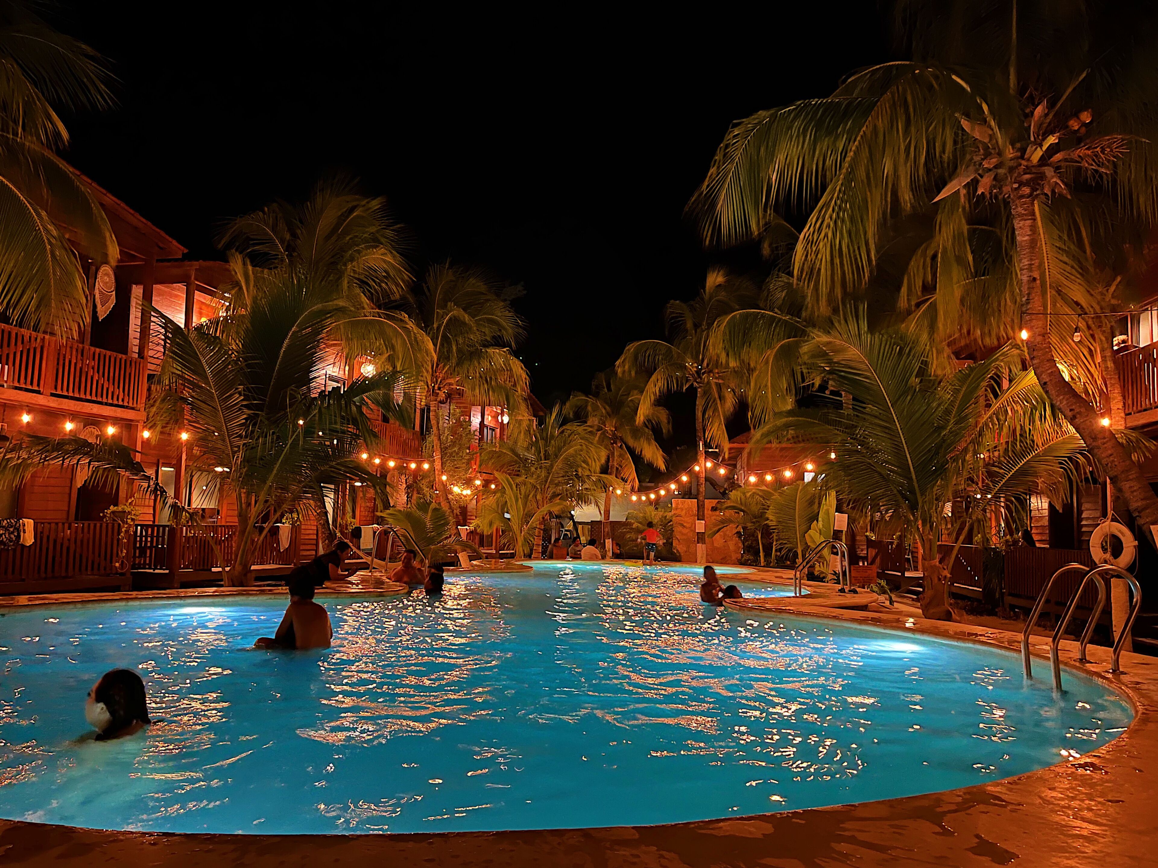 A swimming pool surrounded by palm trees and a building with a balcony.