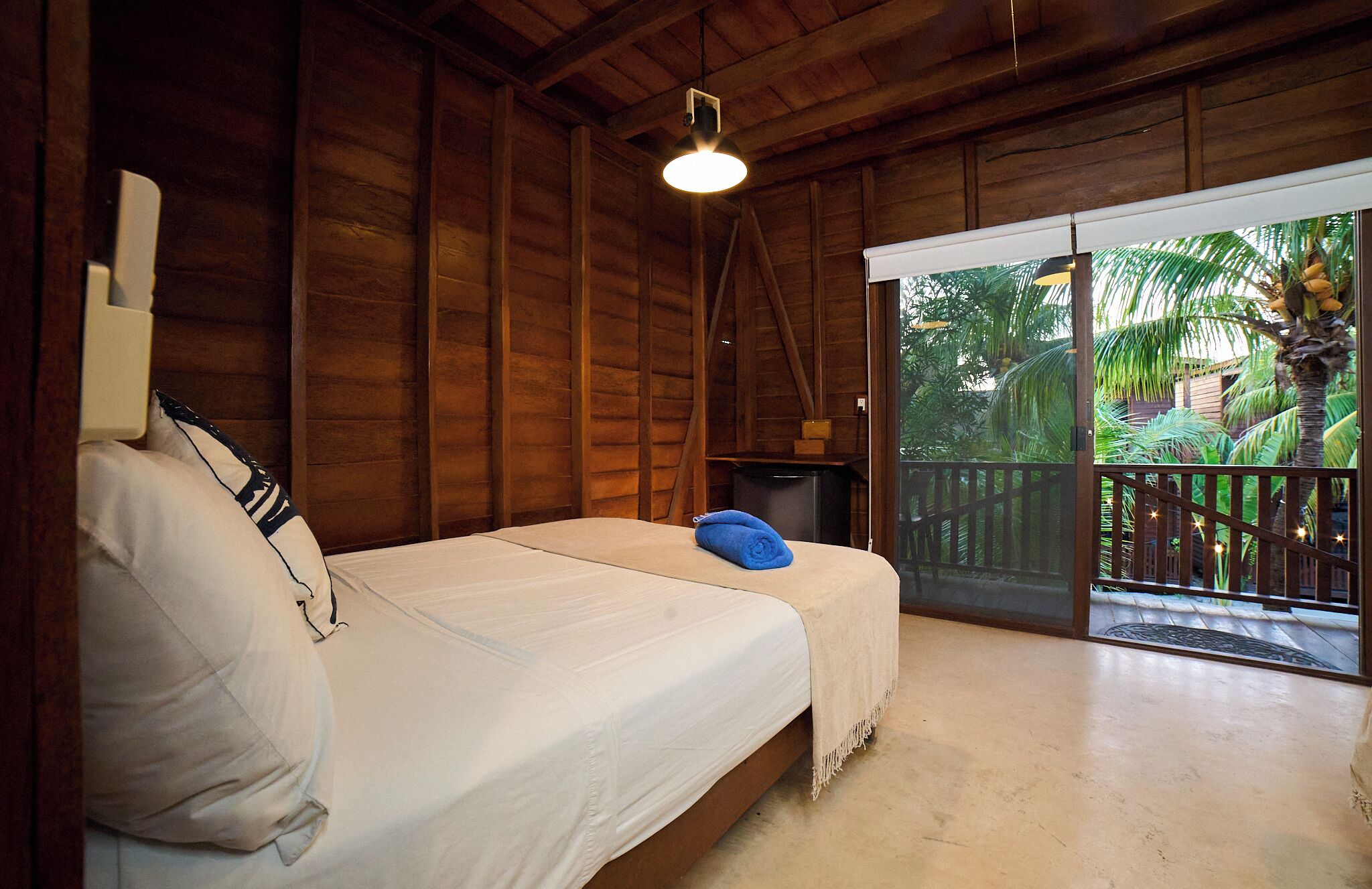 Una habitación con cama, una mesita, una lámpara en el techo y vista a un jardín por una puerta corrediza.