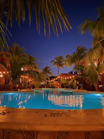 A nighttime pool area with palm trees and string lights, surrounded by buildings.