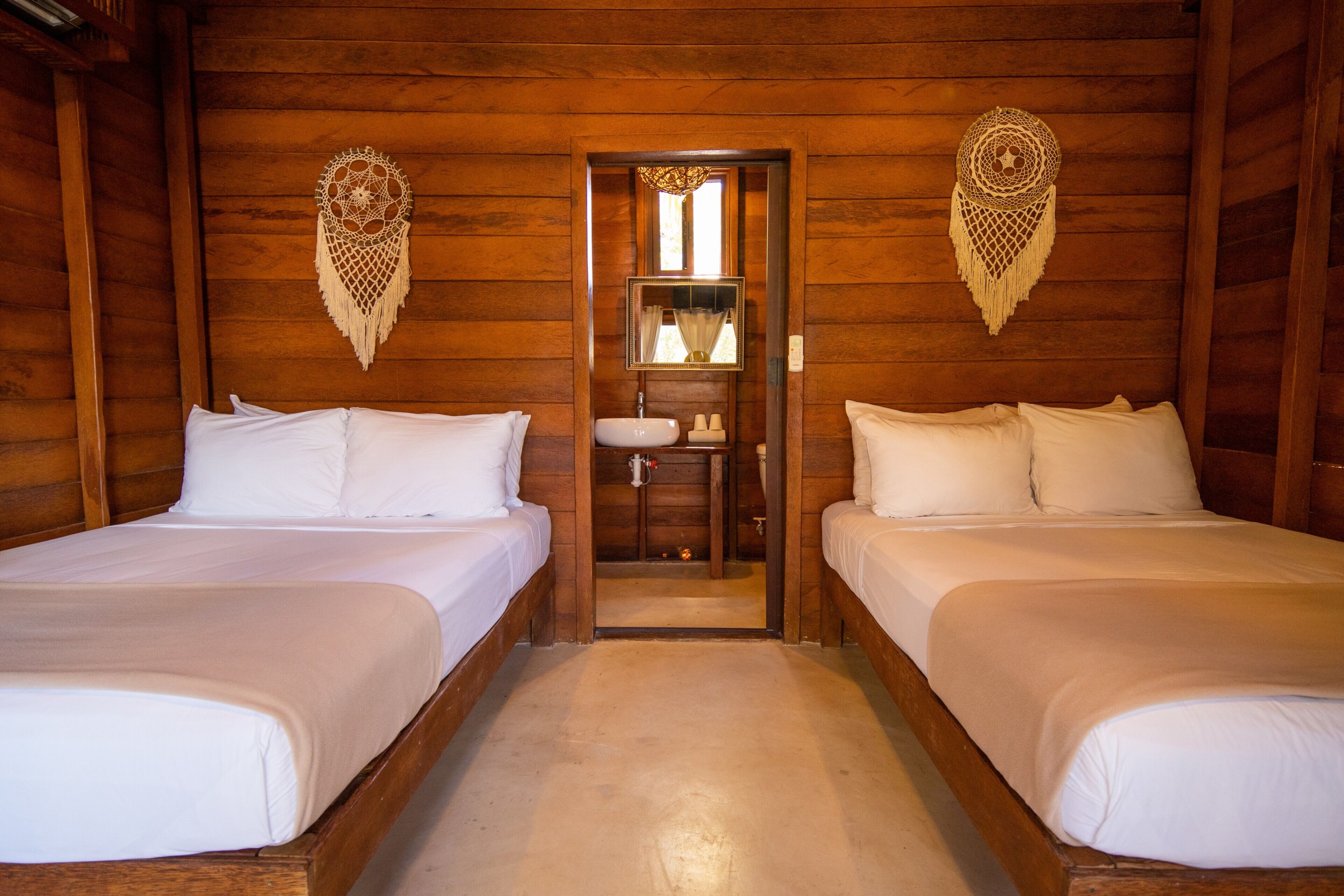 A wooden cabin room with two beds, a small bathroom, and a door leading to another room.