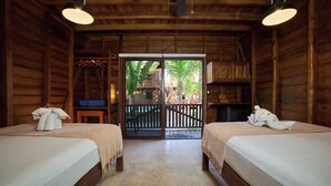 Una habitación tipo cabaña de madera con dos camas, un balcón y vistas a palmeras.